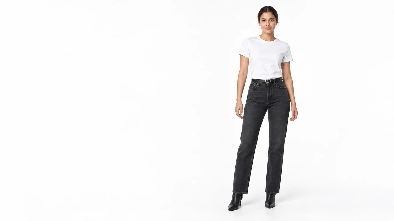 Eine Frau mit weißem T-Shirt, dunkelgrauer Jeans und schwarzen Stiefeletten in einem weißen Studio